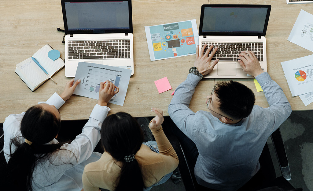 three people with laptops and printed graphs discussing business process management tools