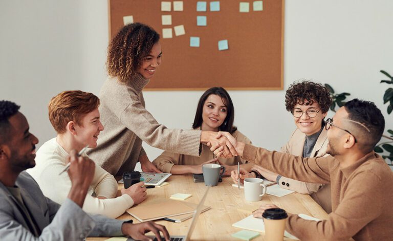 Conservatively dressed young business people shaking hands at a boardroom table after a budget meeting.