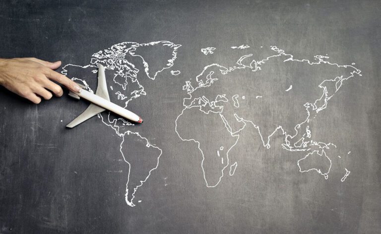 A hand guiding a toy plane across a world map drawn on a chalkboard.